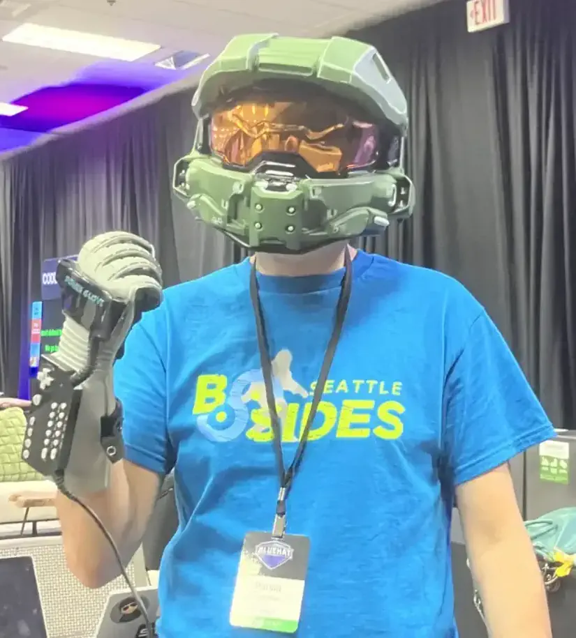 A picture of a person wearing a Halo helmet, a blue BSides Seattle t-shirt and wearing a Nintendo Power Glove on their right hand.