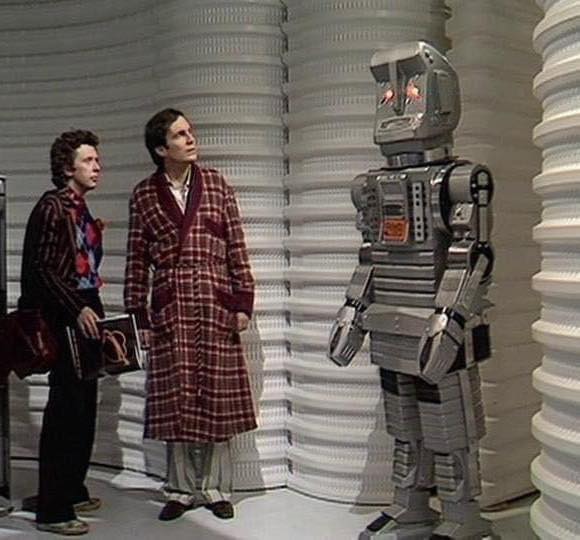 A captured image from The Hitchhiker's Guide to the Galaxy TV series. On the left there are Ford and Arthur, and on the right there is Marvin the paranoid robot.